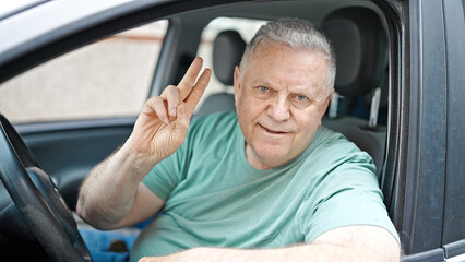 Wall Mural - Middle age grey-haired man smiling confident sitting on car doing victory gesture at street