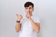 © Krakenimages.com - Young non binary man wearing casual white t shirt asking to be quiet with finger on lips pointing with hand to the side. silence and secret concept.