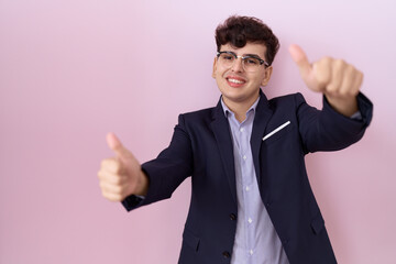 Canvas Print - Young non binary man with beard wearing suit and tie approving doing positive gesture with hand, thumbs up smiling and happy for success. winner gesture.