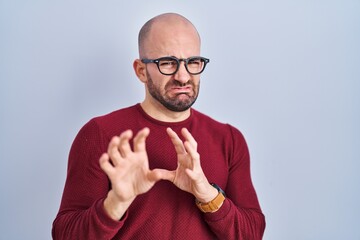 Sticker - Young bald man with beard standing over white background wearing glasses disgusted expression, displeased and fearful doing disgust face because aversion reaction.