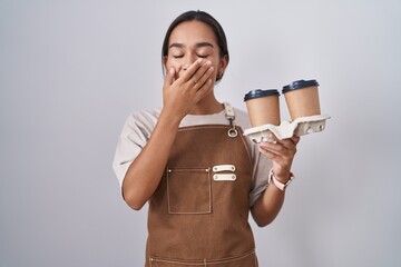 Wall Mural - Young hispanic woman wearing professional waitress apron holding coffee bored yawning tired covering mouth with hand. restless and sleepiness.