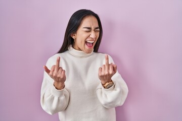 Wall Mural - Young south asian woman standing over pink background showing middle finger doing fuck you bad expression, provocation and rude attitude. screaming excited
