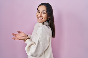 Wall Mural - Young south asian woman standing over pink background pointing aside with hands open palms showing copy space, presenting advertisement smiling excited happy