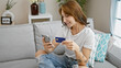 © Krakenimages.com - Young woman shopping with smartphone and credit card sitting on sofa at home