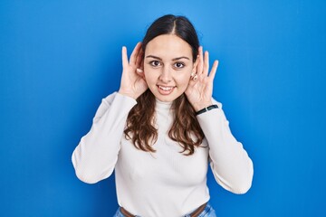 Sticker - Young hispanic woman standing over blue background trying to hear both hands on ear gesture, curious for gossip. hearing problem, deaf