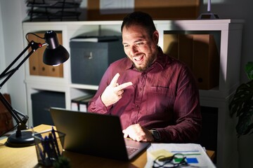 Canvas Print - Plus size hispanic man with beard working at the office at night smiling with happy face winking at the camera doing victory sign. number two.