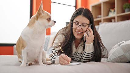 Canvas Print - Young hispanic woman with chihuahua dog speaking on the phone and taking notes lying on the sofa at home