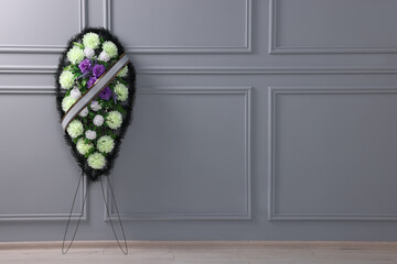 Wall Mural - Funeral wreath of plastic flowers with ribbon near light grey wall indoors, space for text