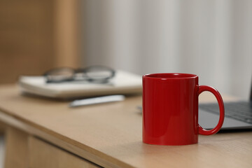 Poster - Red ceramic mug and laptop on wooden table at workplace. Space for text