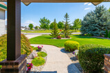 Fototapeta Uliczki - View from the front porch of a modern suburban home with a manicured front lawn in a nice community neighborhood across the street to a park on a sunny summer day.
