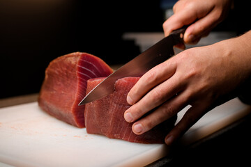 Professional chef neatly cutting part of fresh raw tuna with sharp Japanese knife in restaraunt kitchen