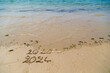 Bonne et heureuse année 2024, élégante carte de voeu montrant la fin de 2023 et le passage à 2024 sur le sable d'une plage et mer turquoise. Slogan à ajouter