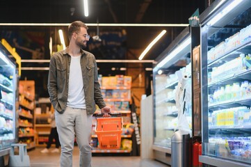 Portrait of smiling handsome man grocery shopping in supermarket, choosing food products from shelf