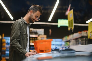 Portrait of smiling handsome man grocery shopping in supermarket, choosing food products from shelf