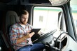 © Serhii - Man truck driver sitting behind wheel of car and holding digital tablet in his hands
