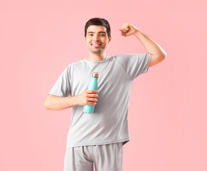 Sticker - Sporty young man with bottle of water showing muscles on pink background