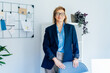 © okrasiuk - Confident middle aged businesswoman standing near grid mood board with pinned plan in office workspace. Portrait of experienced senior female professional, business coach team leader in modern office