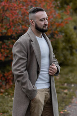 Young handsome man in a trendy coat outdoors. Autumn leaves on background