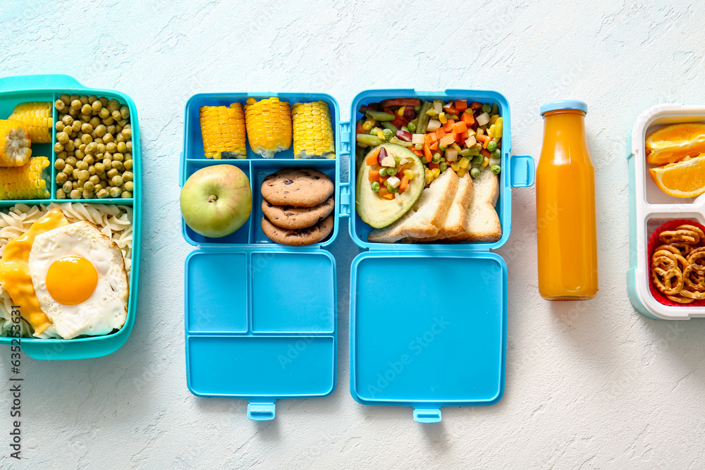 Lunchboxes with different delicious food and bottle of juice on gradient background