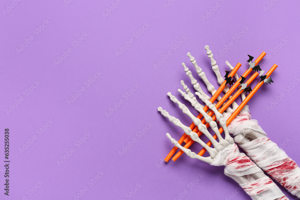 Skeleton hands with straws for Halloween celebration on purple background