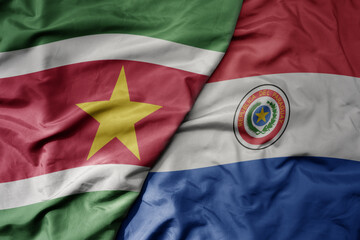 big waving realistic national colorful flag of suriname and national flag of paraguay .