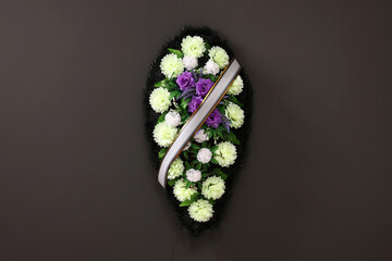 Wall Mural - Funeral wreath of plastic flowers with ribbon hanging on dark grey wall