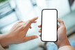© bongkarn - A woman holding a smartphone with a white screen mockup over a blurred cafe in background.
