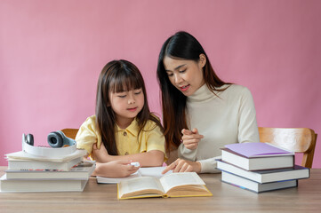 A kind Asian female teacher helps a young, adorable girl read a book and do homework