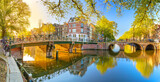 Fototapeta Krajobraz - Panoramic view of Amsterdam in the morning sun. Traditional old houses, bridges and mirror water with reflection. Beautiful morning in Amsterdam.