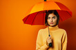 © Anna - Beautiful young woman in a yellow sweater with an umbrella on a orange background.