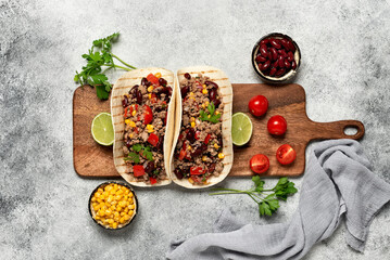 Wall Mural - Mexican tacos with beef on a wooden board. Tacos with ground beef, beans, corn and tomato. Gray rustic background. Top view, flat lay.