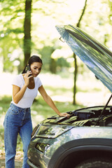 Wall Mural - Young woman standing by broken car on the road and using smartphone calling assistance.