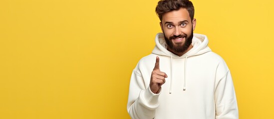 Poster - A bearded man points to empty space offers room for your advertising content in a white hoodie isolated on yellow background
