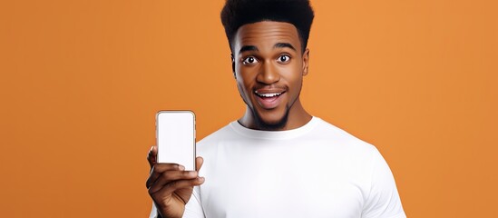 Wall Mural - Surprised African man with short hair holds smartphone with mockup on background