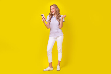 Wall Mural - Full length photo of good mood cheerful woman dressed purple t-shirt look at smartphone on video call isolated on yellow color background