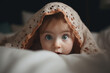 Portrait of a funny caucasian innocent girl peeking out from under the fabric in bed, a pretty little child with big eyes looking at the camera
