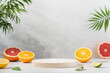 Empty wooden round podium on light grey background surrounded by citrus fruits. Display, pedestal for the presentation of cosmetic products, drinks