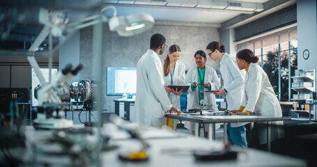 Leinwandbilder - Group of International Multiethnic Lab Specialists Gathering Around a Table to Discuss Blueprints and Components for a High Tech Robotic Project. Young Engineers Working in Company Facility Laboratory