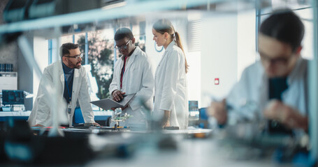 Poster - Diverse Young Group of Engineers Working in a Modern Startup Lab. Male Specialist Soldering a Circuit Board While Team of Professionals Discuss Technological Project Strategy Using Laptop Computer.