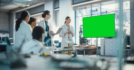 Fototapete - Group of Students Listening to Their Robotics Female Professor Who Uses Green Screen Monitor in a Laboratory. Team of Engineers Having Meeting and Discussing Manufacturing Ideas, Using Technology