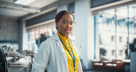Poster - Portrait of Young Smiling Black Woman Wearing Glasses and a Lab Coat Looking at the Camera. Future Engineer Pursuing Scientific Career. Industrial Manufacturing Student in University Laboratory Posing