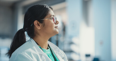 Poster - Profile Portrait Close Up of Young Indian Female Specialist Wearing Lab Coat and Glasses. Professional and Successful Woman Working as an Engineer, Science Student in University Laboratory Posing