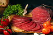 Whole and sliced bresaola on a metal round tray with tomatoes, garlic and parsley