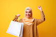 © Goffkein - Happy smiling joyful satisfied muslim woman with paper shopping bag on yellow background