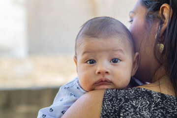 Young Latina mom sitting in a park, holding her newborn baby