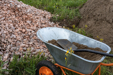 Two-wheeled wheelbarrow with a shovel inside, farming tool, agriculture equipment, heaps of sand and crushed rock, rubble.