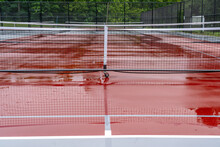 New Portable Pickleball Nets On A Wet Red Tennis Court With White Lines Combined With Gray Pickleball Lines