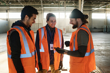 Leinwandbilder - Three happy young male workers of warehouse discussing presentation points while one of them holding tablet and scrolling through slides