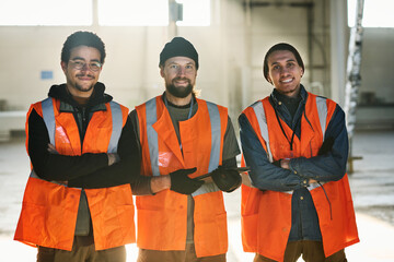 Leinwandbilder - Three young successful engineers of industrial factory or workers of warehouse in safety vests crossing their arms by chest and looking at you
