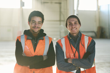 Leinwandbilder - Two happy young multietnic foremen or workers of warehouse in safety jackets standing in front of camera with sunlight on background